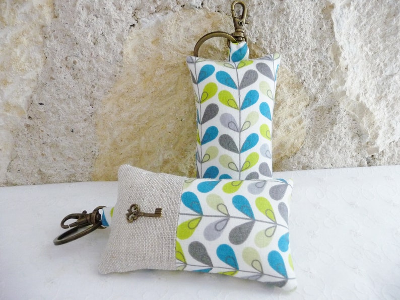 May include: Two keychains with a fabric design of teal, green, and gray leaves on a white background. One keychain has a key attached to it.