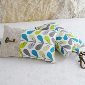 May include: Two keychains with a linen fabric and a blue, green, and gray leaf pattern. One keychain has a small antique key charm.
