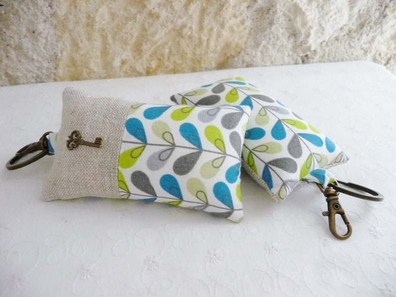 May include: Two keychains with a linen fabric and a blue, green, and gray leaf pattern. One keychain has a small antique key charm.