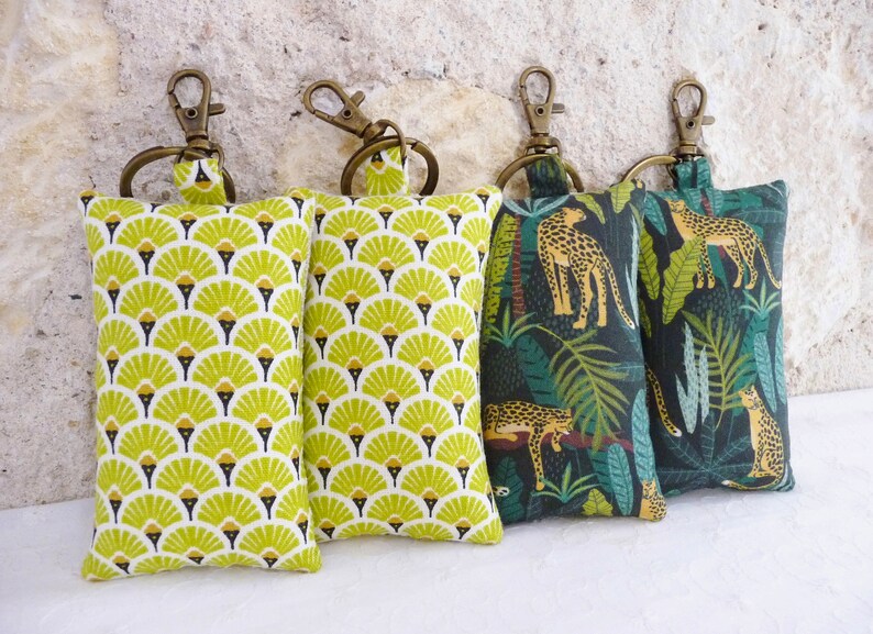 May include: Four keychains with different fabric patterns. Two keychains feature a green and yellow geometric pattern. The other two keychains feature a dark green background with a jungle pattern of leaves and leopards.