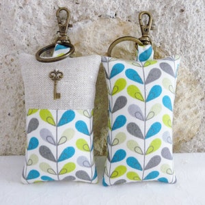 May include: Two keychains with fabric pouches. One pouch is beige linen with a vintage key charm and the other is white with a teal, green, and gray leaf pattern.