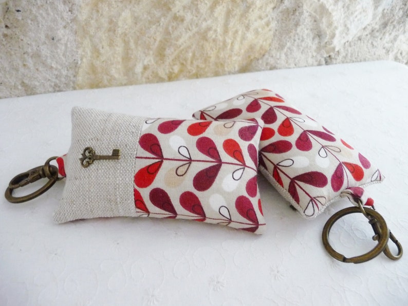 May include: Two keychains with a red, white, and brown floral pattern. One keychain has a small key attached to it.
