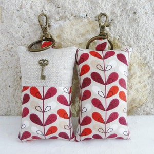 May include: Two keychains with a beige linen fabric and a red, white, and black geometric pattern. One keychain has a small antique key charm.