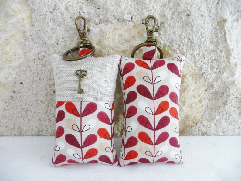 May include: Two keychains with a beige linen fabric and a red, white, and black geometric pattern. One keychain has a small antique key charm.