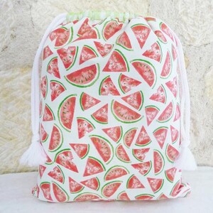 May include: White drawstring bag with a watermelon print. The bag is made of fabric and has a white drawstring closure. The watermelon print is red and green and features watermelon slices.