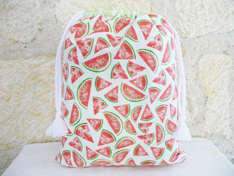 May include: White drawstring bag with a watermelon print. The bag is made of fabric and has a white drawstring closure. The watermelon print is red and green and features watermelon slices.