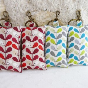 May include: Four keychains with fabric pouches. The pouches are beige with a repeating pattern of red, teal, and green leaves. The keychains are attached to the top of the pouches with a silver ring.