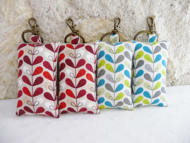May include: Four keychains with fabric pouches. The pouches are beige with a repeating pattern of red, teal, and green leaves. The keychains are attached to the top of the pouches with a silver ring.