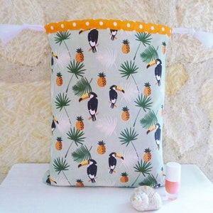 May include: A green drawstring bag with a white and orange polka dot trim. The bag features a tropical print with toucans, pineapples, and palm leaves.