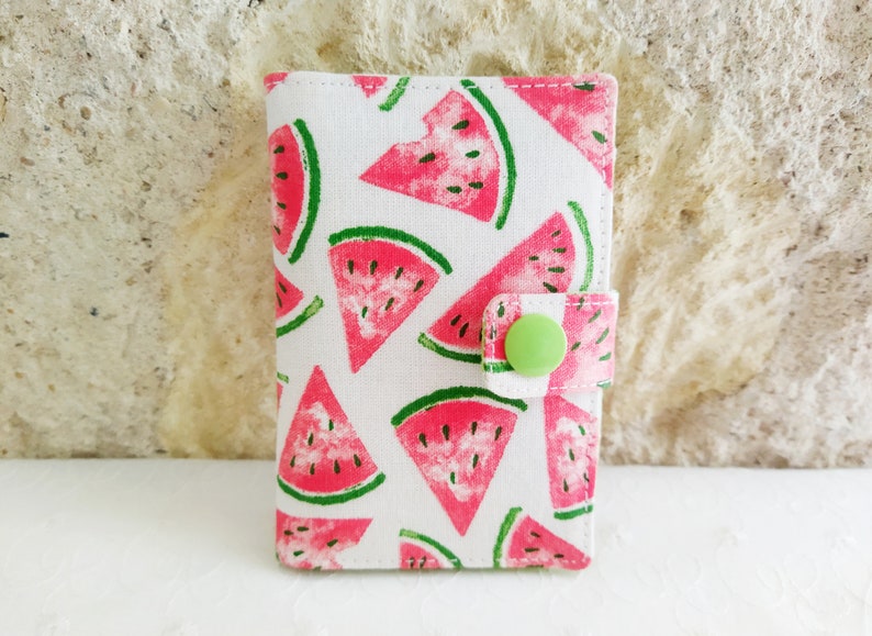 May include: A small white fabric wallet with a watermelon print and a green button closure.