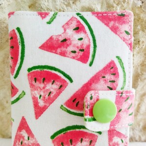 May include: A white fabric wallet with a watermelon print and a green button closure.