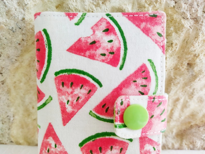 May include: A white fabric wallet with a watermelon print and a green button closure.