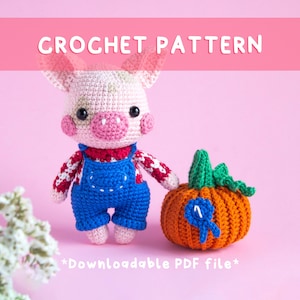 Puede incluir: Un cerdo tejido a ganchillo con un peto azul y una camisa roja, con una calabaza naranja tejida a ganchillo. El cerdo tiene orejas, mejillas y hocico rosas. La calabaza tiene un tallo verde y una cinta azul. El texto "CROCHET PATTERN" y "*Downloadable PDF file*" son visibles.