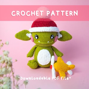 May include: A crocheted green goblin doll wearing a red and white hat with a pink pom-pom. The doll has white ears with pink accents and is holding a yellow crocheted airplane. The text "CROCHET PATTERN" and "*Downloadable PDF file*" are displayed.