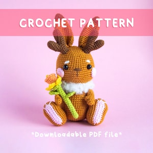 Könnte beinhalten: Häkelanleitung für einen braunen Hasen mit Geweih, der eine gelbe Blume hält. Das Muster ist als PDF-Datei herunterladbar. *Herunterladbare PDF-Datei*