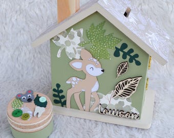 Peut inclure: Une tirelire en bois en forme de maison peinte en vert sauge avec une illustration de faon, des découpes de feuilles et le prénom Louison. À côté se trouve une petite boîte ronde en bois décorée d'une tête de souris, de boutons et d'une dent.