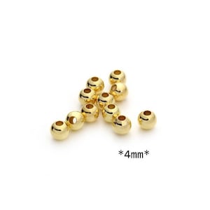 Puede incluir: Un conjunto de cuentas doradas brillantes, cada una de aproximadamente 4 mm de diámetro, sobre un fondo blanco. Las cuentas tienen una superficie lisa y reflectante, con un agujero en el centro. El texto "*4mm*" está incluido.
