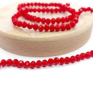 Op de afbeelding: Een streng rode gefacetteerde glazen kralen. De kralen zijn klein en rond en zijn geregen op een doorzichtige draad.