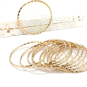 May include: A set of 12 gold-toned bangle bracelets with a twisted design. The bracelets are stacked on top of each other.