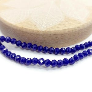 May include: A strand of dark blue faceted glass beads. The beads are small and round, and they are strung together on a clear thread.