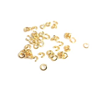Peut inclure: Un ensemble de petits anneaux de jonction et d'anneaux ouverts de couleur dorée, dispersés sur une surface blanche. Les anneaux sont de tailles et de formes variées, certains fermés et d'autres ouverts, pour la création de bijoux ou l'artisanat.