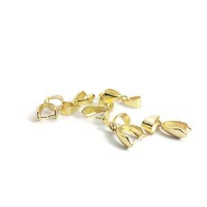 May include: A collection of gold-coloured jewellery clasps are arranged on a white background. Each clasp features a rounded, open-ended design with a small loop. The clasps are made of a shiny, metallic material.