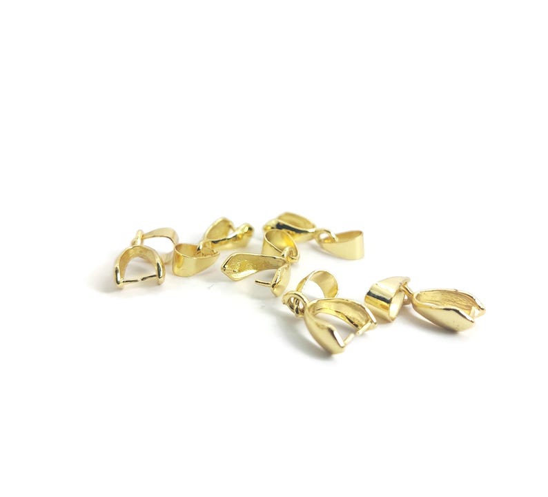 May include: A collection of gold-coloured jewellery clasps are arranged on a white background. Each clasp features a rounded, open-ended design with a small loop. The clasps are made of a shiny, metallic material.