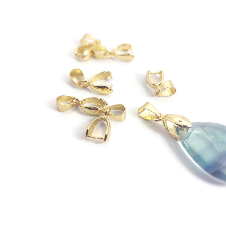 May include: A collection of gold-coloured pendant bails are displayed on a white background. One bail is attached to a blue and green stone pendant. The bails have a loop and a hinged clasp for attaching to a chain or cord.