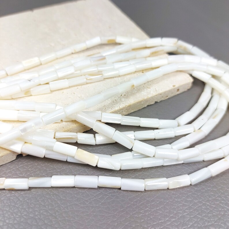May include: A strand of white rectangular shell beads. The beads are smooth and have a slight iridescent sheen.