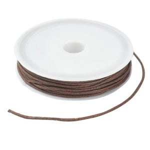 Peut inclure: Une bobine de fil de coton ciré marron. Le fil est enroulé autour d'une bobine en plastique blanc. Le fil est déroulé de la bobine et repose sur un fond blanc. Idéal pour la fabrication de bijoux, l'artisanat et les projets de bricolage.