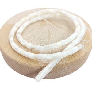 Può includere: Un filo di perline bianche di conchiglia, ogni perlina è di forma quadrata con una finitura leggermente iridescente.