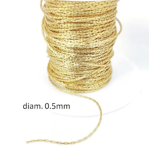 Peut inclure: Bobine de cordon métallique doré, de 0,5 mm de diamètre, enroulée serrée. Le cordon a un aspect texturé et tissé. Le texte "diam. 0.5mm" est imprimé sur l'image. Parfait pour la création de bijoux et l'artisanat.