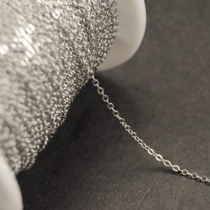 Könnte beinhalten: Eine Spule mit silberner Kette, von der ein Stück Kette abgeht. Die Kette ist fein, zart und von der Art Kabelkette.