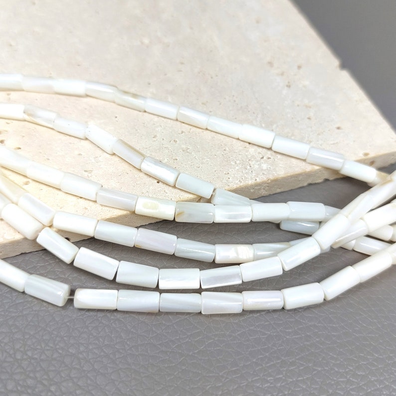 May include: A strand of white shell beads, each bead is a rectangular prism shape.