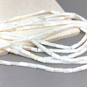 May include: A strand of white mother of pearl beads. The beads are rectangular in shape and have a smooth, polished finish.