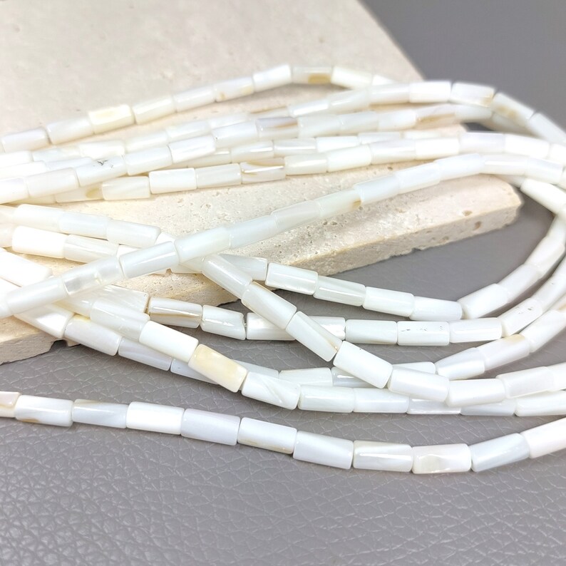 May include: A strand of white mother of pearl beads. The beads are rectangular in shape and have a smooth, polished finish.