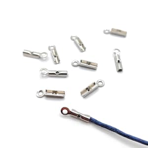 May include: Silver metal cord end caps with a small loop on the top. The cord end caps are scattered on a white surface. One cord end cap is attached to a blue cord.