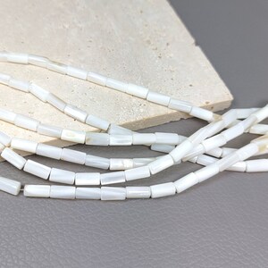 May include: A strand of white mother of pearl beads, each bead is a rectangular shape with a slightly rounded edge.