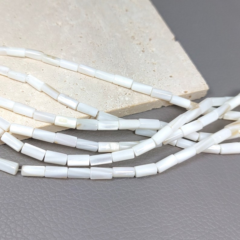 May include: A strand of white mother of pearl beads, each bead is a rectangular shape with a slightly rounded edge.