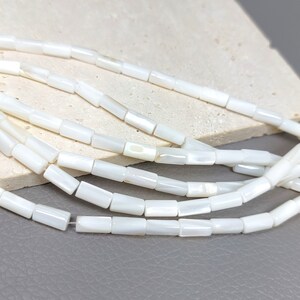 May include: A strand of white shell beads with a rectangular shape. The beads have a slight iridescent sheen.
