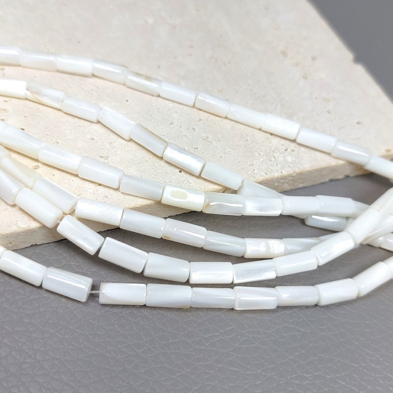 May include: A strand of white shell beads with a rectangular shape. The beads have a slight iridescent sheen.