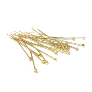Peut inclure: Un groupe d'épingles à tête ronde de couleur dorée. Les épingles sont disposées de manière aléatoire sur un fond blanc.