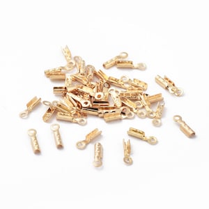 May include: A pile of gold-colored metal crimp end caps for jewelry making. The caps have a small loop on one end and a flat, crimped end on the other.