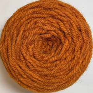 May include: A close-up of a ball of orange yarn. The yarn is wound tightly and has a soft, fuzzy texture.