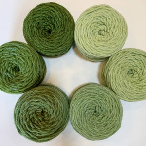 May include: Six balls of yarn in various shades of green. The yarn is wound into balls and arranged in a circle.