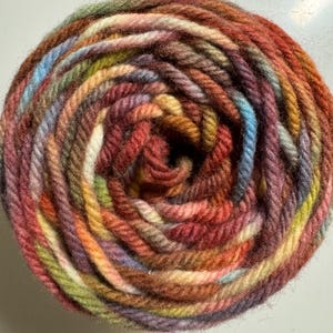 May include: A tightly wound ball of yarn in a variety of colors, including red, orange, yellow, green, blue, and purple. The yarn appears to be a blend of fibers, creating a textured appearance. Ideal for knitting and crocheting projects.
