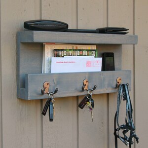 May include: Gray wooden wall mounted key holder with three hooks, a shelf for mail and a smaller shelf for other items. The key holder has a copper finish on the hooks.