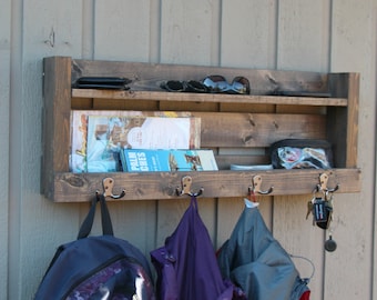 May include: Rustic wooden wall mounted shelf with two shelves and hooks. The shelf has a brown stain and is holding various items, including sunglasses, books, and keys.