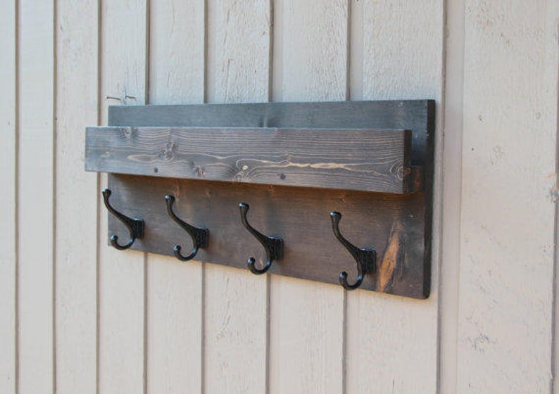 Pu&ograve; includere: Un appendiabiti in legno rustico con uno scaffale e quattro ganci in metallo nero. L'appendiabiti &egrave; tinto di un colore marrone scuro e ha una finitura invecchiata.