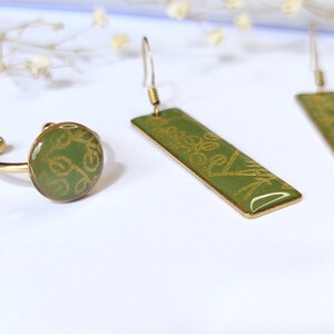 May include: A set of gold-tone jewelry featuring a ring and a pair of earrings. The ring and earrings have a green background with a gold floral pattern.